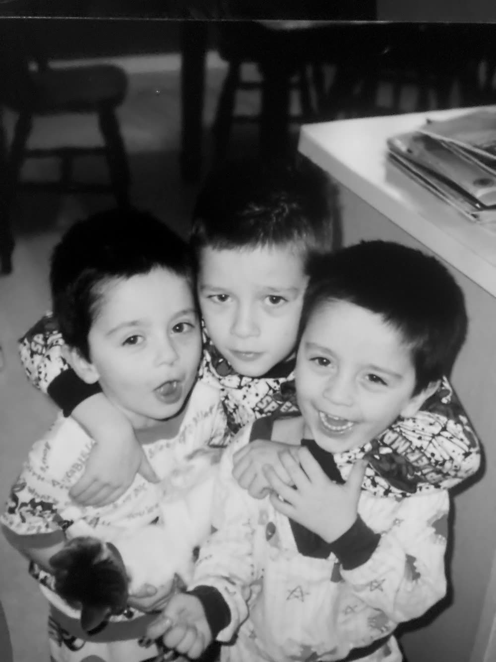 Three young brothers in cartoon pyjamas with their arms around each other.