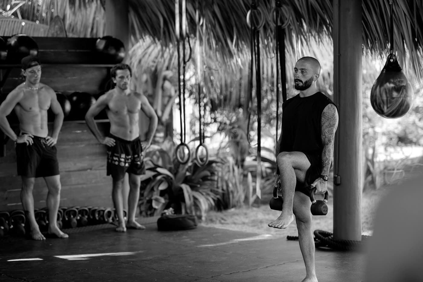 A coach demonstrating a single-leg movement with two kettlebells while two people watch.