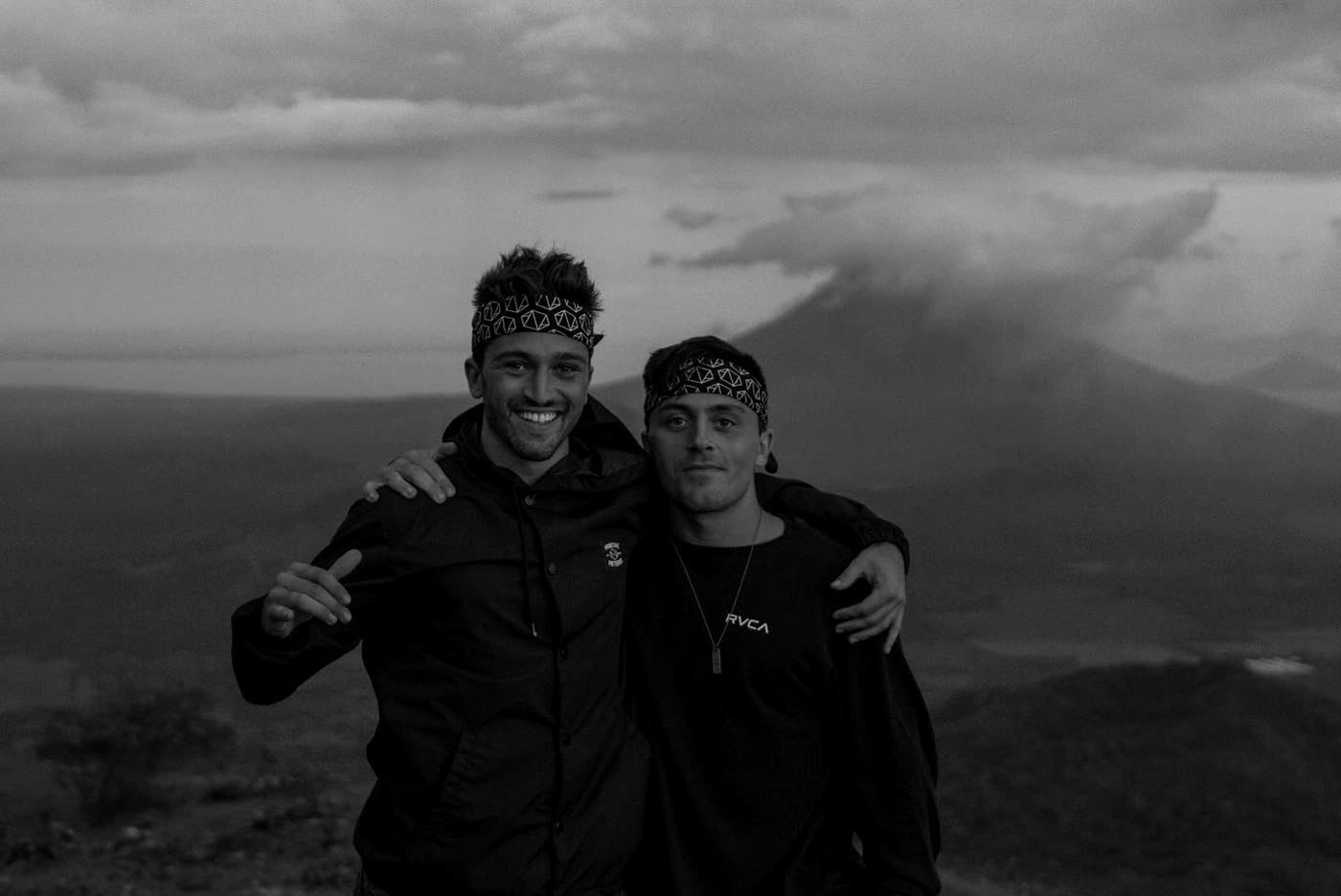 Two of the brothers on a ridge at dusk with a volcano behind them.
