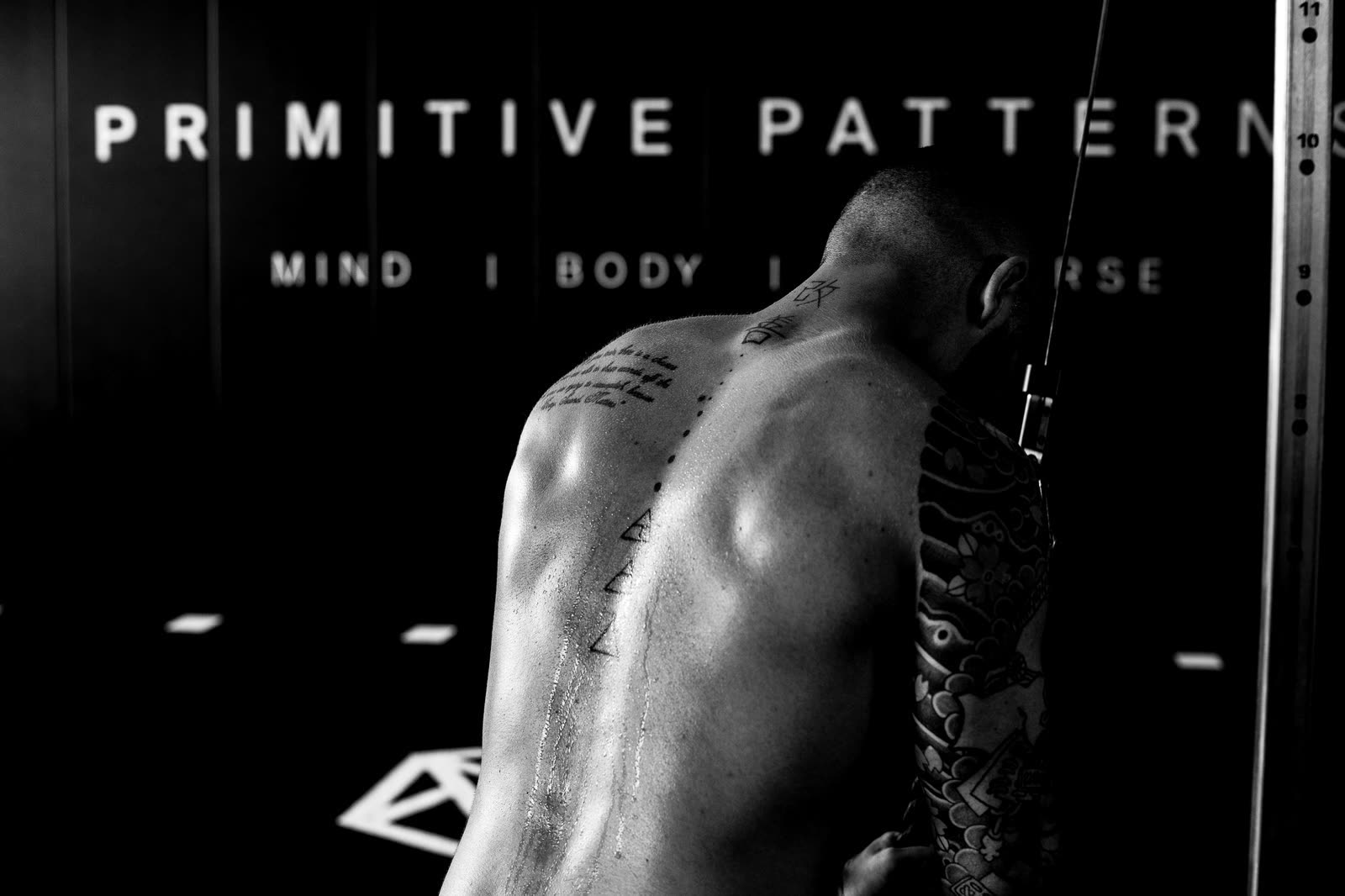 A man training in front of a gym wall reading Primitive Patterns, Mind Body Universe.
