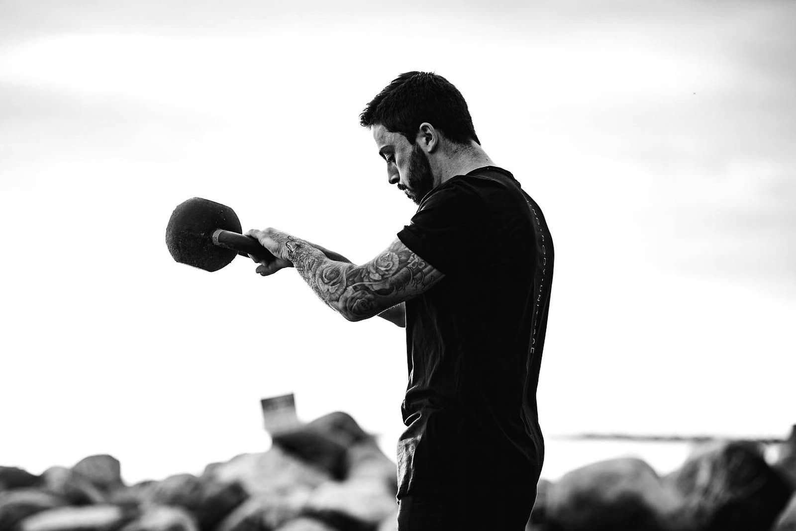 A man in a black shirt holding a sledgehammer against a bright open sky.