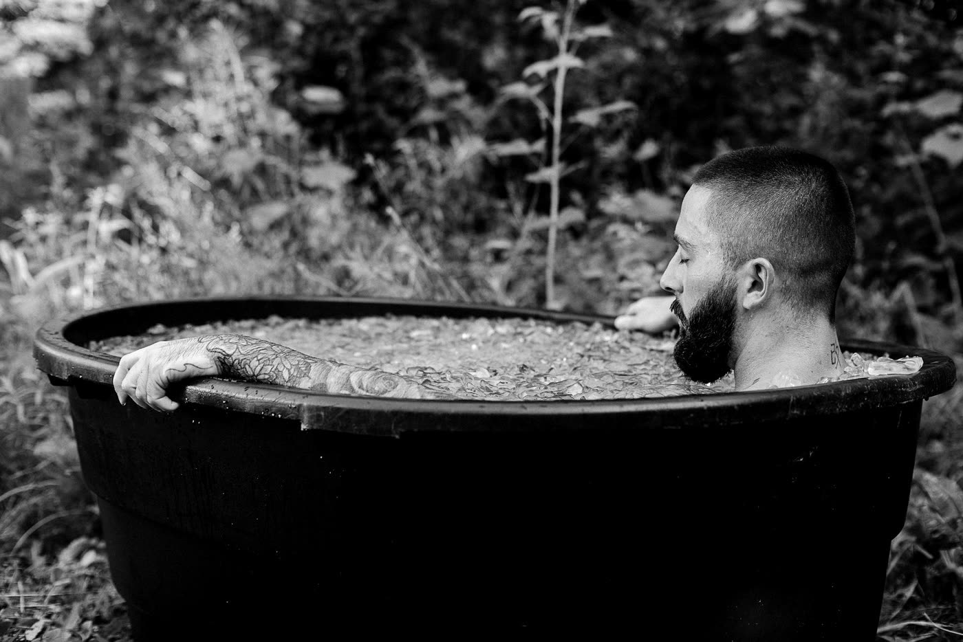A bearded man submerged to the shoulders in an ice bath.