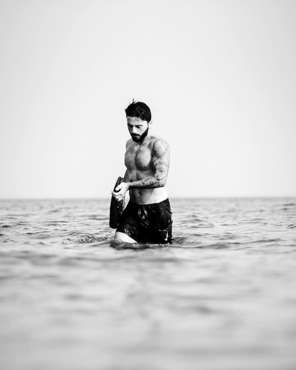 A man standing alone waist-deep in flat open ocean under an empty sky.
